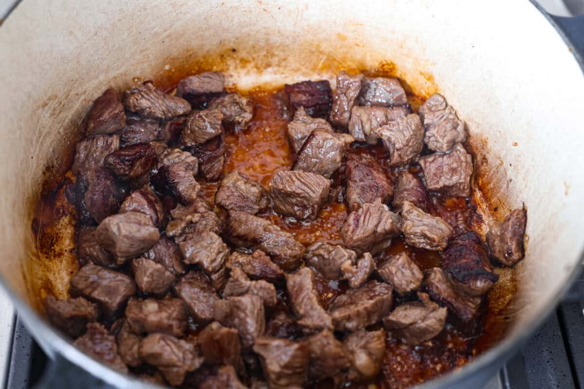 My one pot beef and rice has tender beef, fluffy rice, carrots, and warm spices all cooked in one pot. But one special ingredient is the secret to its incredible flavor. Keep reading to find out what it is! Cubed beef browning in the bottom of the dutch oven.