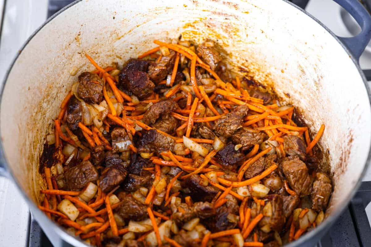 My one pot beef and rice has tender beef, fluffy rice, carrots, and warm spices all cooked in one pot. But one special ingredient is the secret to its incredible flavor. Keep reading to find out what it is! Carrots, onions and seasonings aded to the dutch oven with the beef.