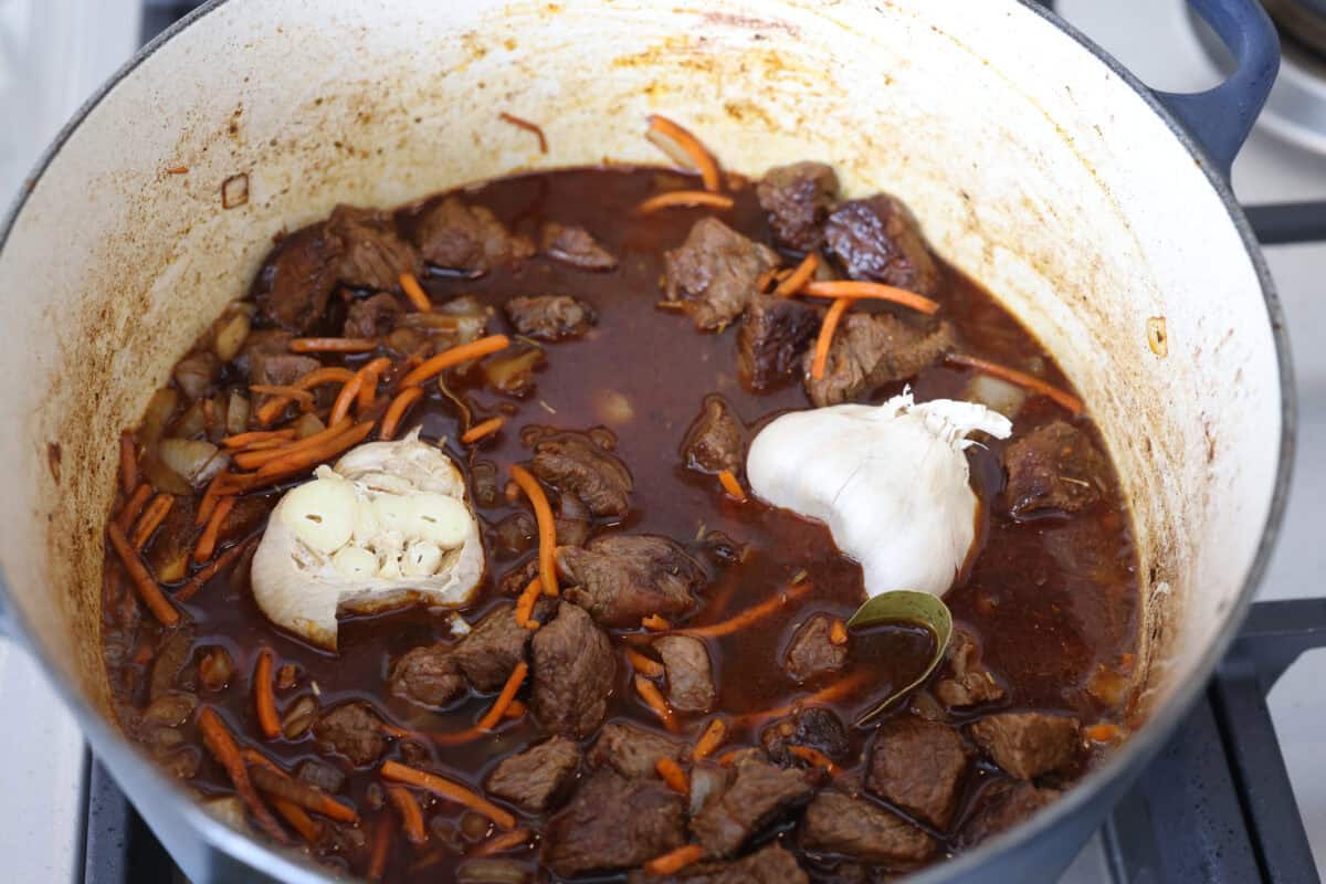 My one pot beef and rice has tender beef, fluffy rice, carrots, and warm spices all cooked in one pot. But one special ingredient is the secret to its incredible flavor. Keep reading to find out what it is! Beef broth and garlic heads added to the dutch oven.