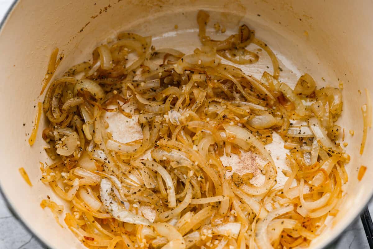 I had to try Stanley Tucci’s pasta fagioli, and his shortcut is so smart! He uses marinara sauce to add tons of flavor without a long list of ingredients. Add creamy beans, tender pasta, kale, and Parmesan, and you have a cozy dinner in just 35 minutes. Onions, seasonings and garlic cooking in the bottom of a dutch oven.