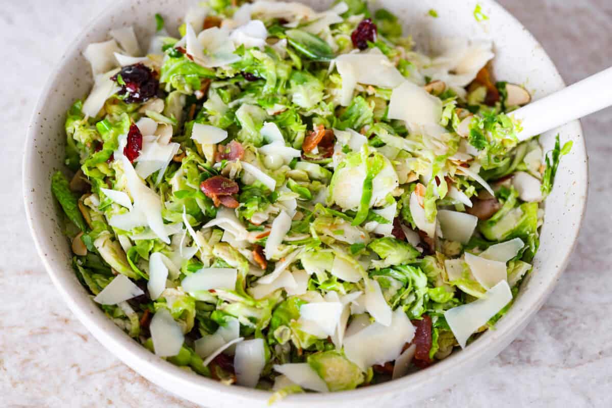 I didn’t always get excited about Brussels sprouts, but this Brussels sprouts salad with bacon changed that. Crispy bacon, tart cranberries, toasted almonds, and Parmesan make every bite so good, with a warm maple-orange dressing to tie it all together. Dressing and parmesan cheese added to the warm Brussels sprouts salad with bacon and mixed together.