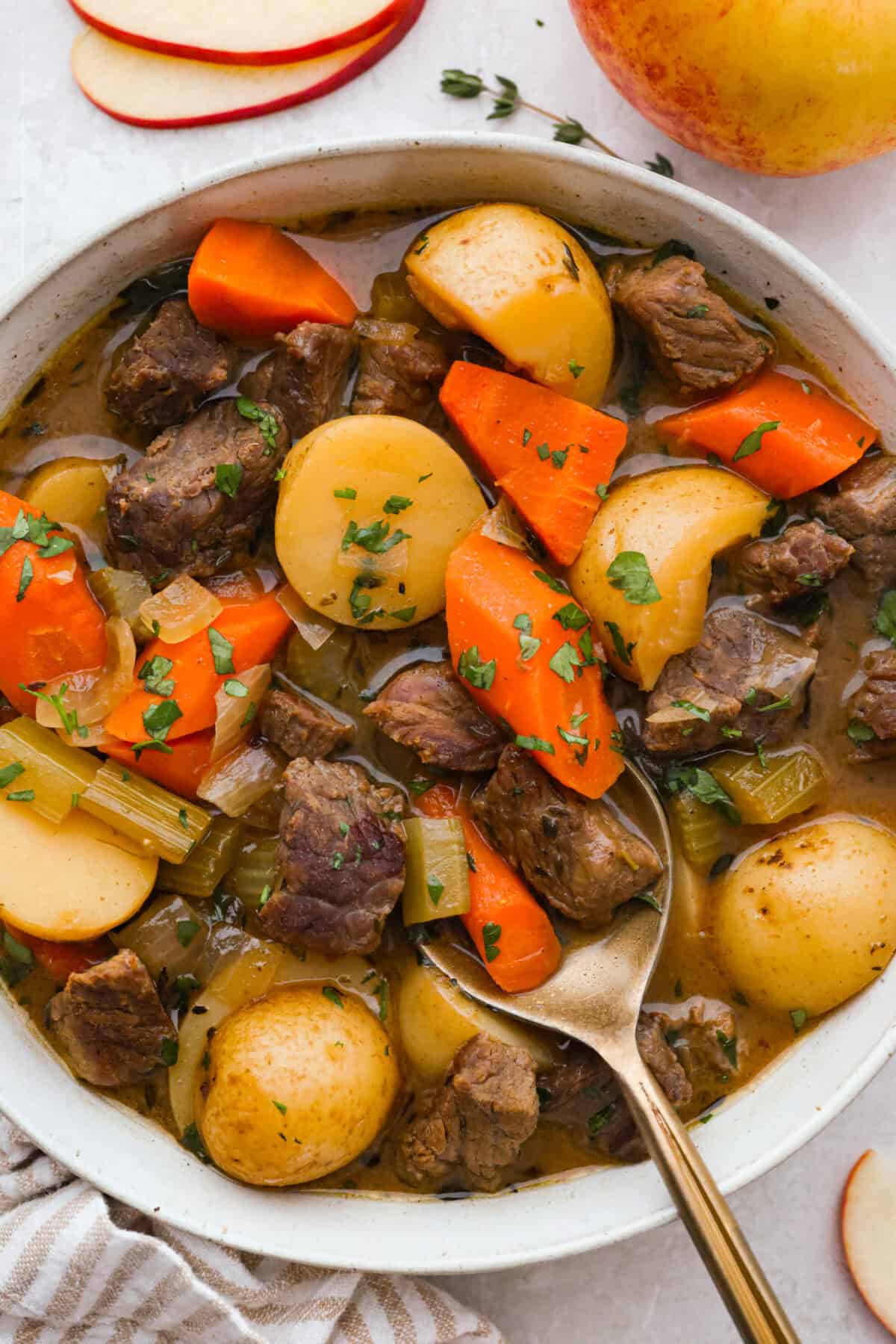 Apple cider beef stew tastes like fall by the spoonful! Tender beef, buttery potatoes, and hearty veggies simmer in a rich broth with apple cider, thyme, and sage for the coziest cold-weather dinner. Bowl of apple cider beef stew with a gold spoon.