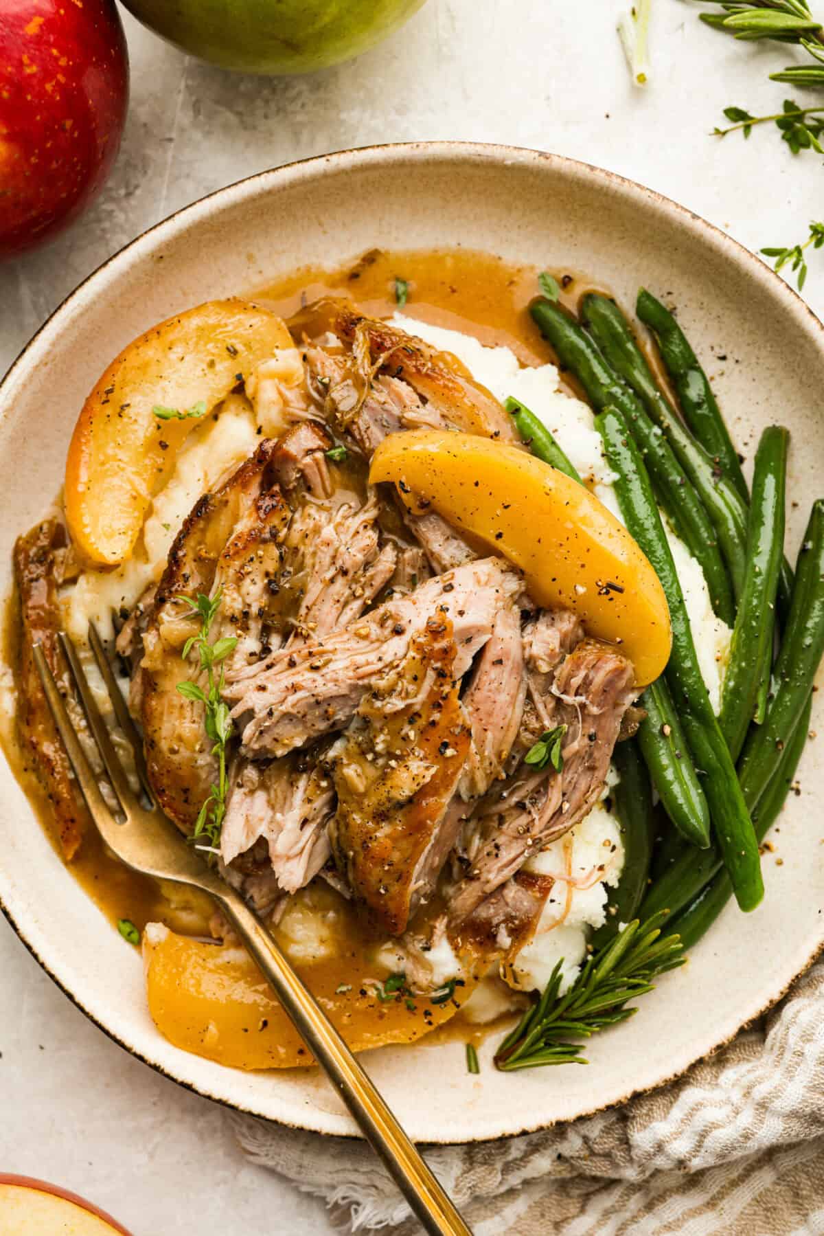 If you love a good Sunday roast, this apple cider pork roast needs to be on your fall menu. Tender pork cooks with apple cider, herbs, and sweet-tart apples until it’s fall-apart tender and perfect over creamy mashed potatoes. Serving size of apple cider pork roast over mashed potatoes and next to green beans.