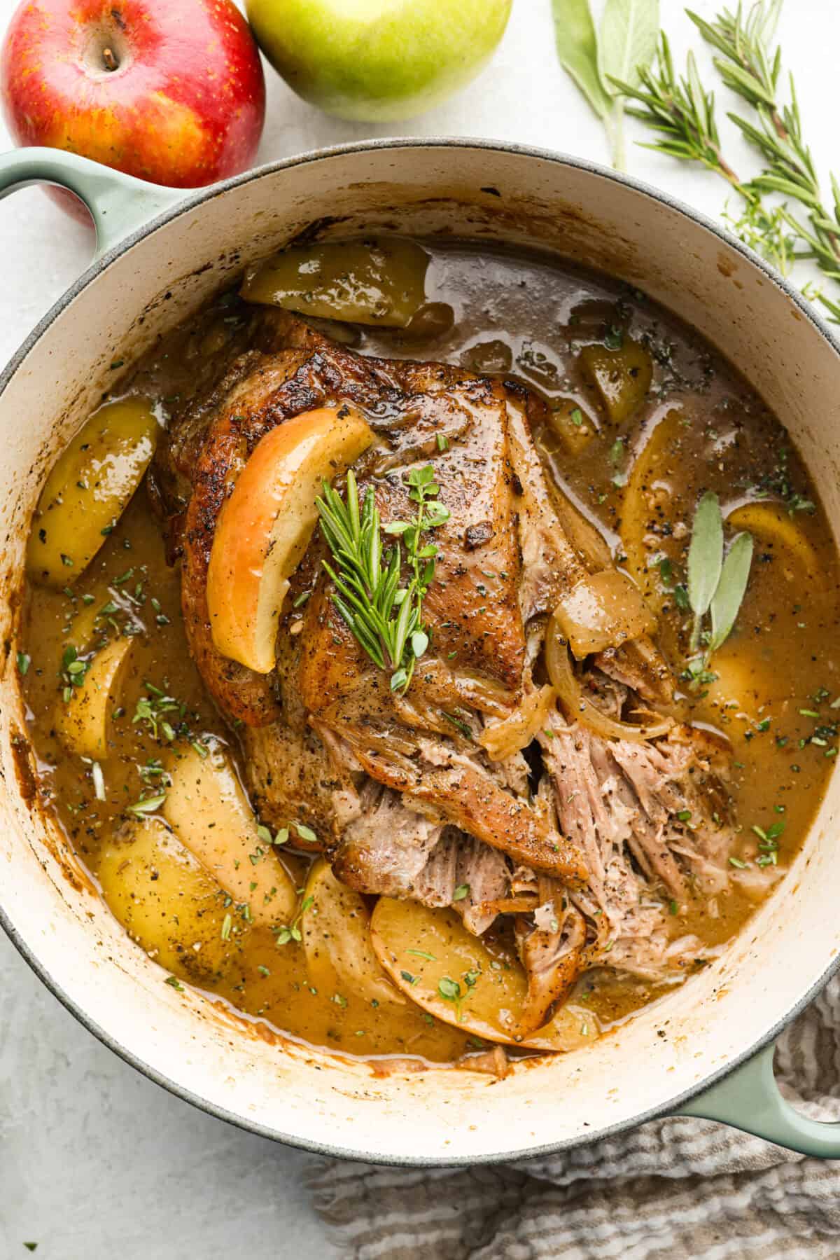 If you love a good Sunday roast, this apple cider pork roast needs to be on your fall menu. Tender pork cooks with apple cider, herbs, and sweet-tart apples until it’s fall-apart tender and perfect over creamy mashed potatoes. Dutch oven with cooked apple cider pork roast garnished with fresh herbs.