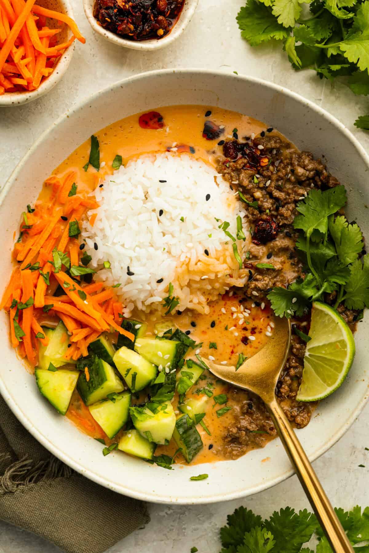 I kept seeing beef broth bowls all over social media, so of course I had to make my own! This easy version has savory ground beef, warm rice, crunchy veggies, and a creamy coconut curry broth. Top down shot of a beef broth bowl garnished with lime, chili crisp, and cilantro.