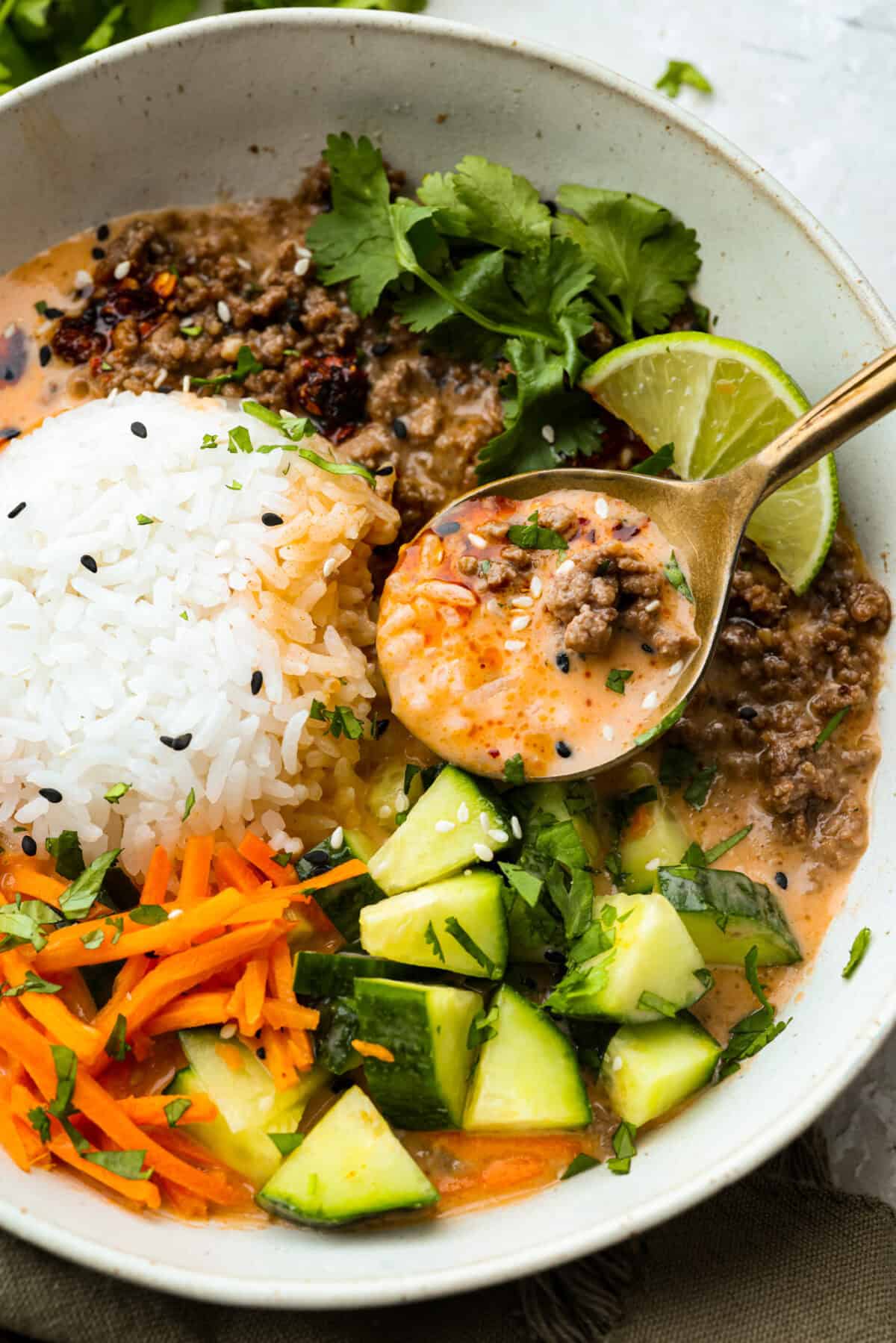I kept seeing beef broth bowls all over social media, so of course I had to make my own! This easy version has savory ground beef, warm rice, crunchy veggies, and a creamy coconut curry broth. Close up shot of the prepared beef broth bowl with someone lifting a spoonful of it out.