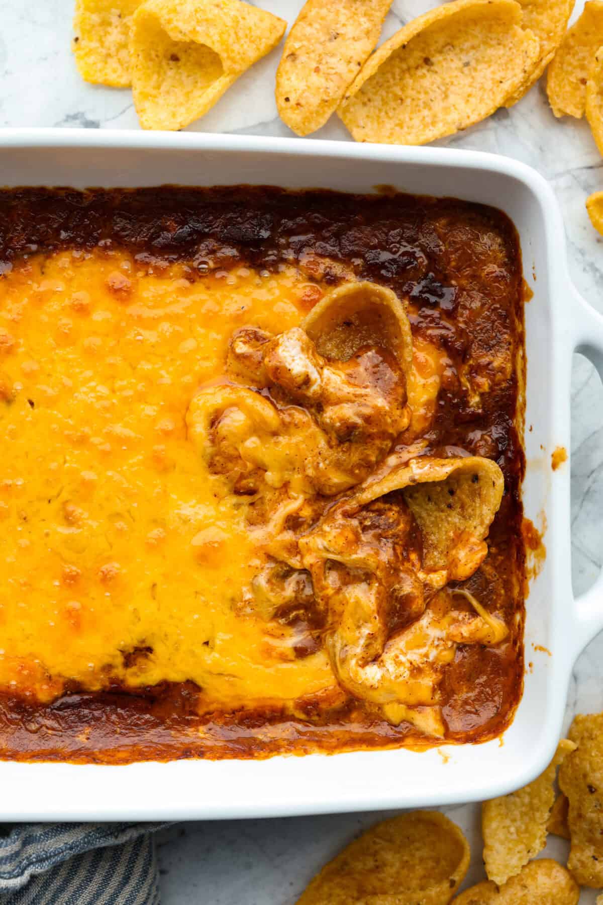 Cincinnati chili dip is the easiest game day appetizer you didn’t know you needed! Also called Skyline dip, it has just three ingredients: cream cheese, Cincinnati-style chili, and melty cheddar cheese. Top down shot of Cincinnati chili dip with a coupe of chips in it.