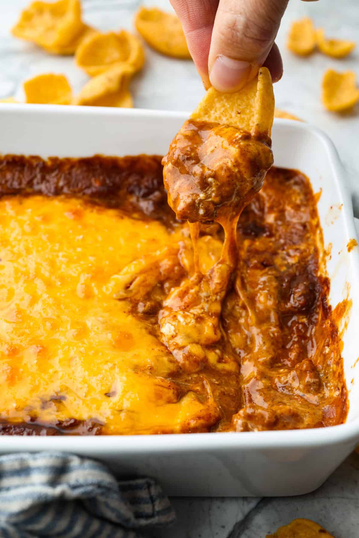 Cincinnati chili dip is the easiest game day appetizer you didn’t know you needed! Also called Skyline dip, it has just three ingredients: cream cheese, Cincinnati-style chili, and melty cheddar cheese. Someone getting a scoop of Cincinnati chili dip with a scoop style corn chip.