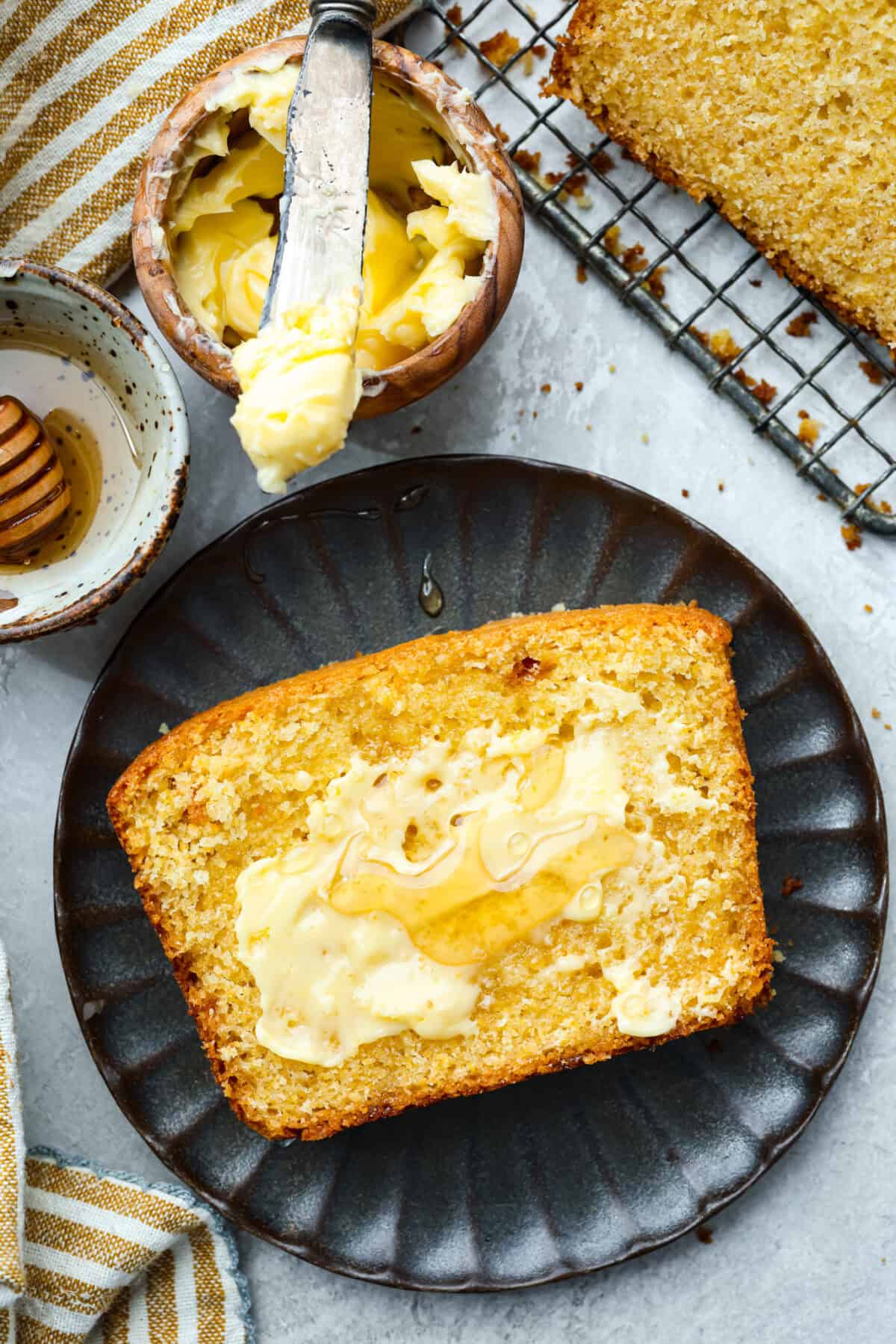 Plated slice of cornbread spread with butter and honey. 