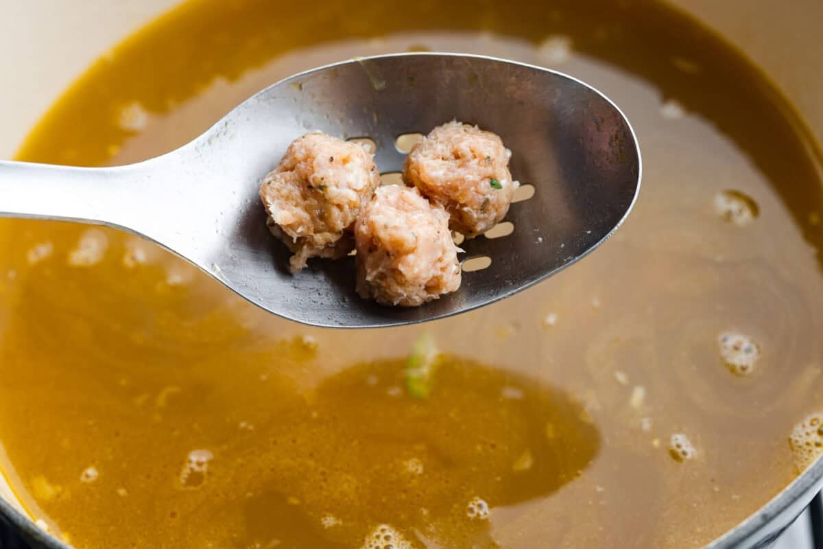 There’s a lot to love about Italian wedding soup! Tender chicken meatballs, vegetables, tiny pasta, and spinach come together in a savory broth for a simple meal that’s hearty, flavorful, and easy to make. Meatballs being added to the soup.
