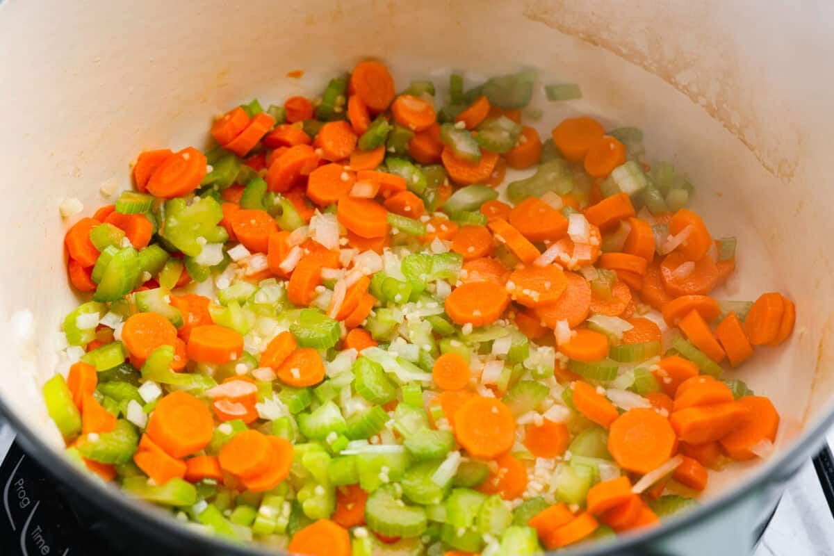 There’s a lot to love about Italian wedding soup! Tender chicken meatballs, vegetables, tiny pasta, and spinach come together in a savory broth for a simple meal that’s hearty, flavorful, and easy to make. Carrots, onion, celery and garlic cooking in a pot.