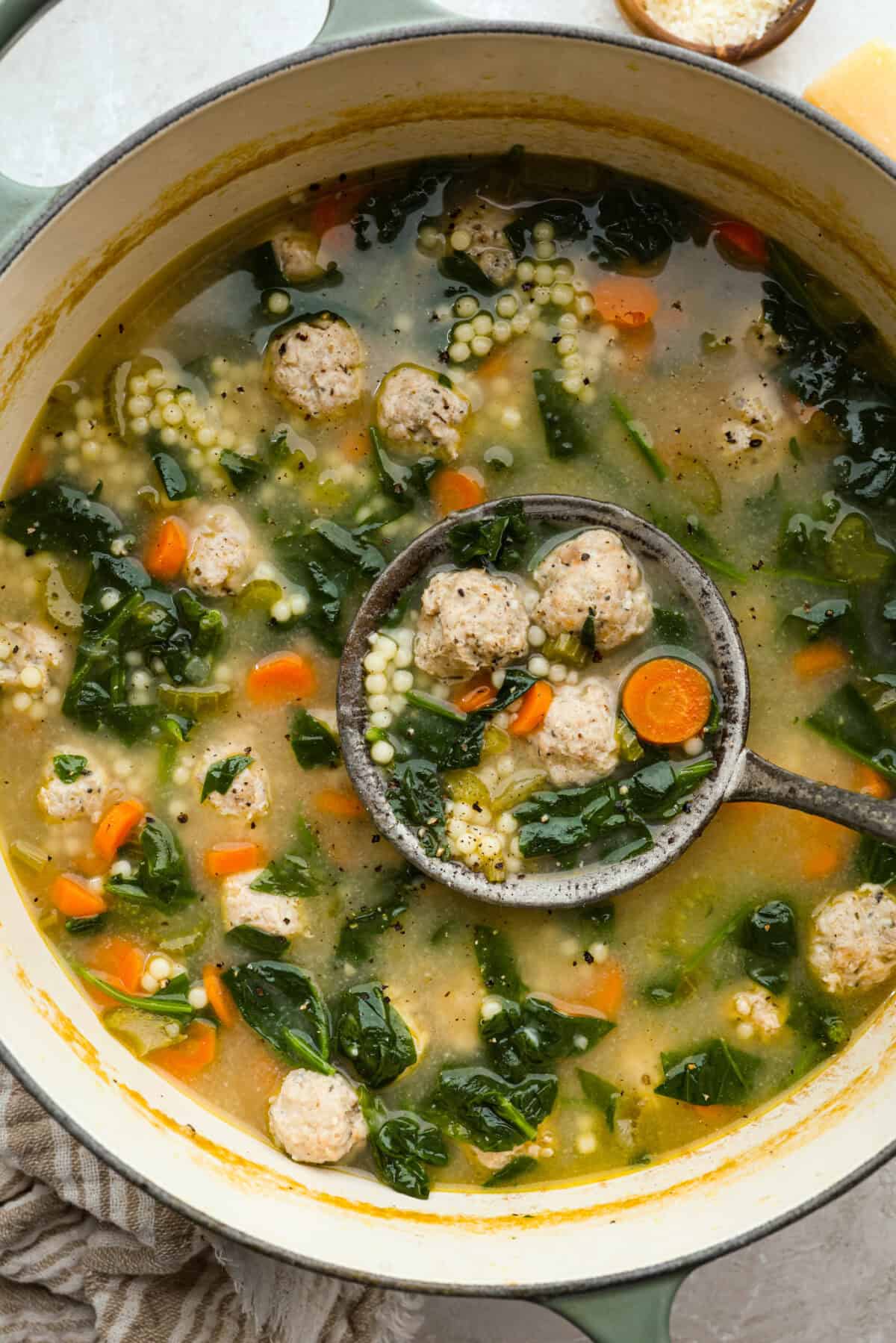 There’s a lot to love about Italian wedding soup! Tender chicken meatballs, vegetables, tiny pasta, and spinach come together in a savory broth for a simple meal that’s hearty, flavorful, and easy to make. Large pot of Italian wedding soup, with a vintage ladle.