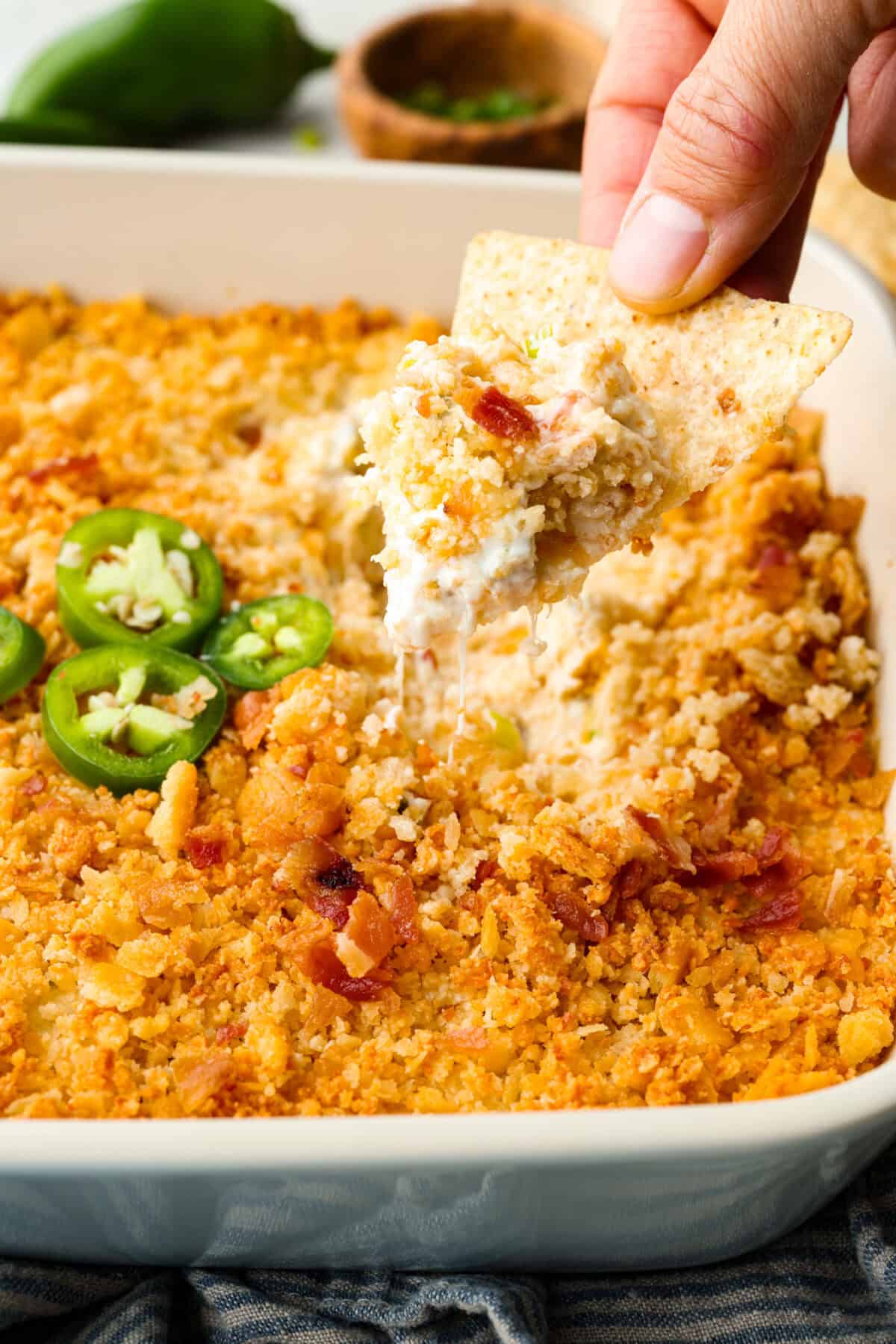 Someone using a chip to scoop some of the jalapeño popper dip out of the baking dish. 