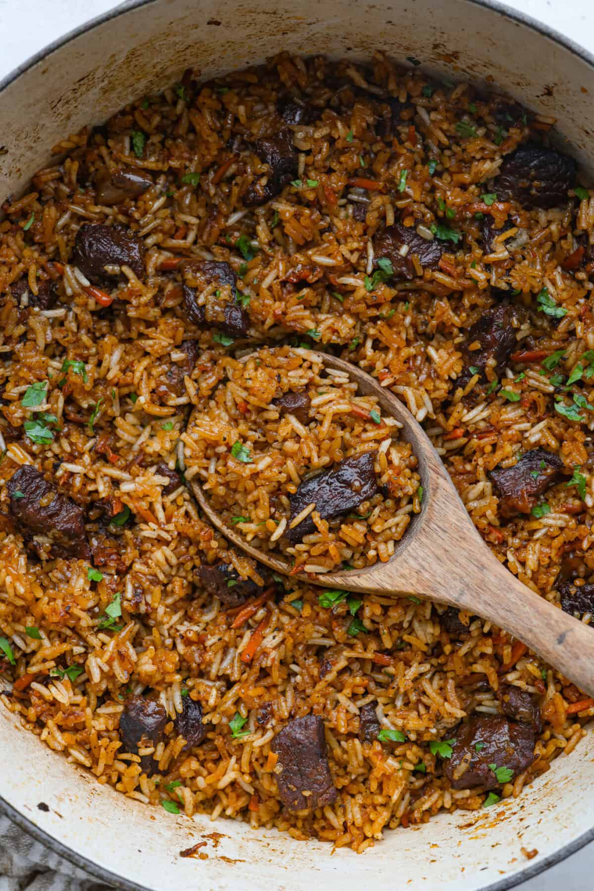 My one pot beef and rice has tender beef, fluffy rice, carrots, and warm spices all cooked in one pot. But one special ingredient is the secret to its incredible flavor. Keep reading to find out what it is! Dutch oven with one pot beef and rice all cooked with a large wooden serving spoon.