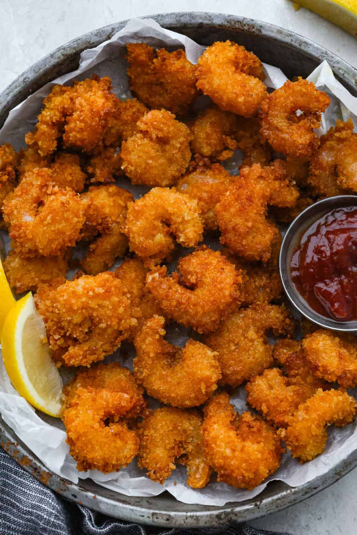 These crispy popcorn shrimp are little bites of golden, crunchy goodness! Juicy shrimp get coated in seasoned panko and fried until perfectly crisp. Serve them hot with a squeeze of lemon and cocktail sauce for dipping! Plater of crispy popcorn shrimp with lemon wedges and cocktail sauce.