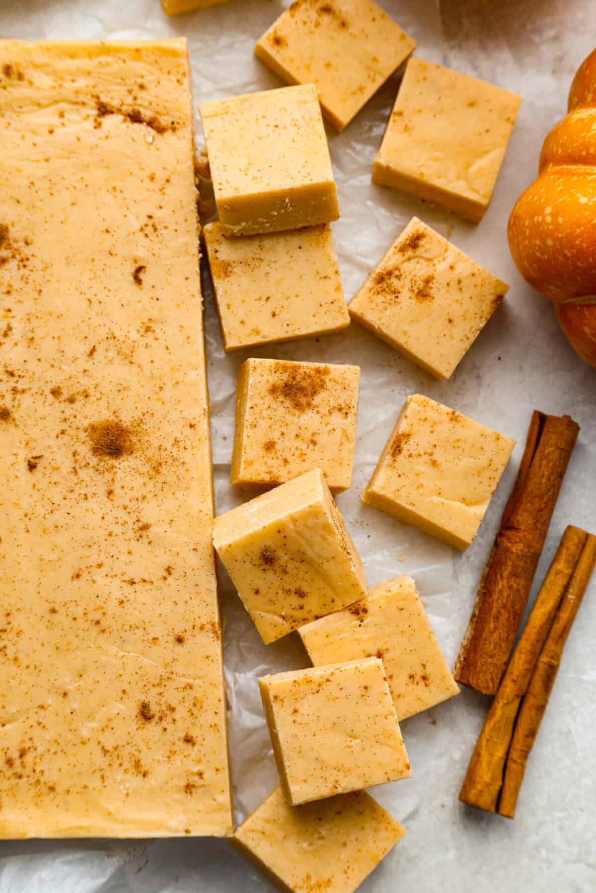 4-ingredient pumpkin fudge is the perfect treat when I want something sweet with a pumpkin-spice vibe. Four simple ingredients and a few minutes of prep make this creamy fall favorite. Overhead shot of pumpkin fudge cut into squares with sticks of cinnamon next to them.