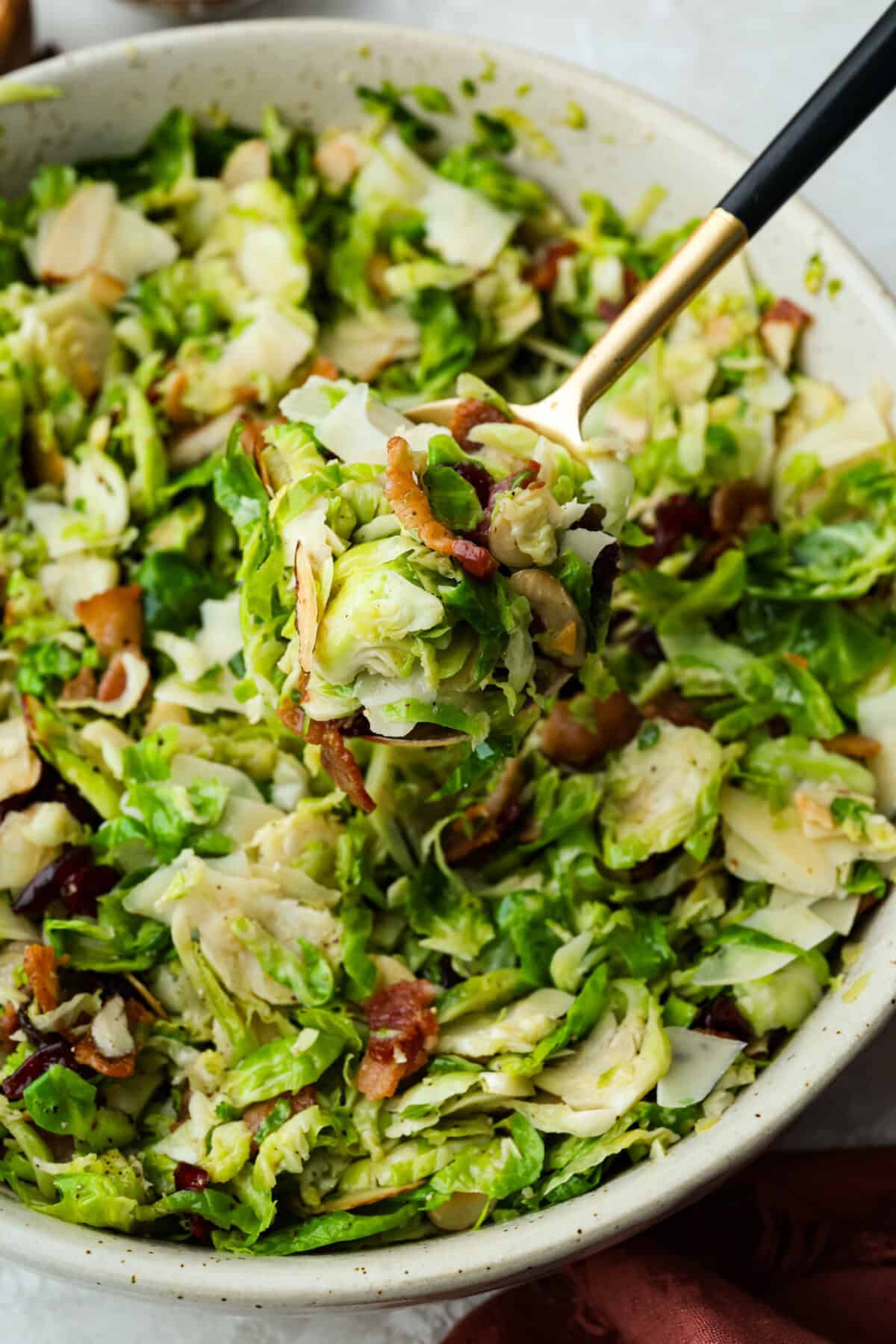 I didn’t always get excited about Brussels sprouts, but this Brussels sprouts salad with bacon changed that. Crispy bacon, tart cranberries, toasted almonds, and Parmesan make every bite so good, with a warm maple-orange dressing to tie it all together. Someone lifting a large spoonful of warm Brussels sprouts salad with bacon out of the large serving bowl.
