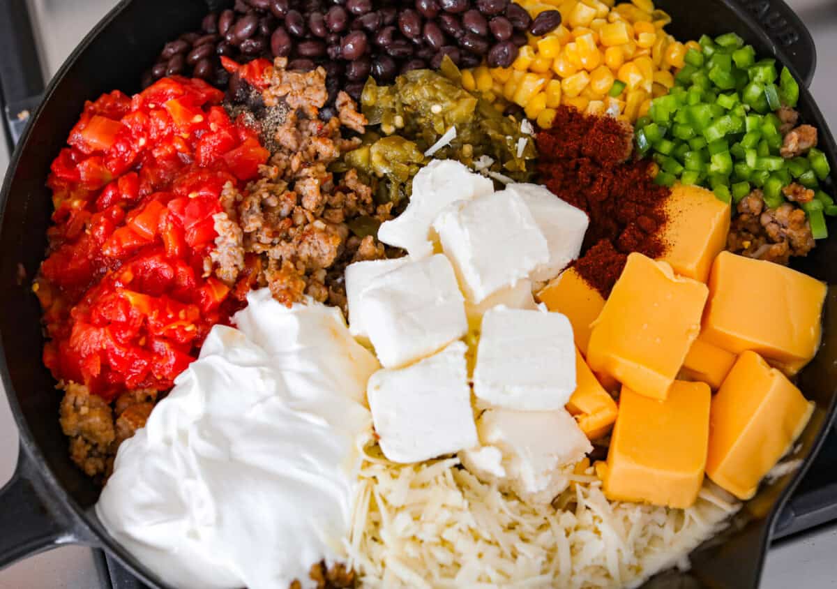 My hot cowboy dip is what I'm bringing to the next game day party! It's loaded with savory sausage, gooey cheese, and a little kick from the jalapeños. Everything comes together in one skillet, so there's less cleanup and more time to dig in! All of the ingredients added to the skillet.