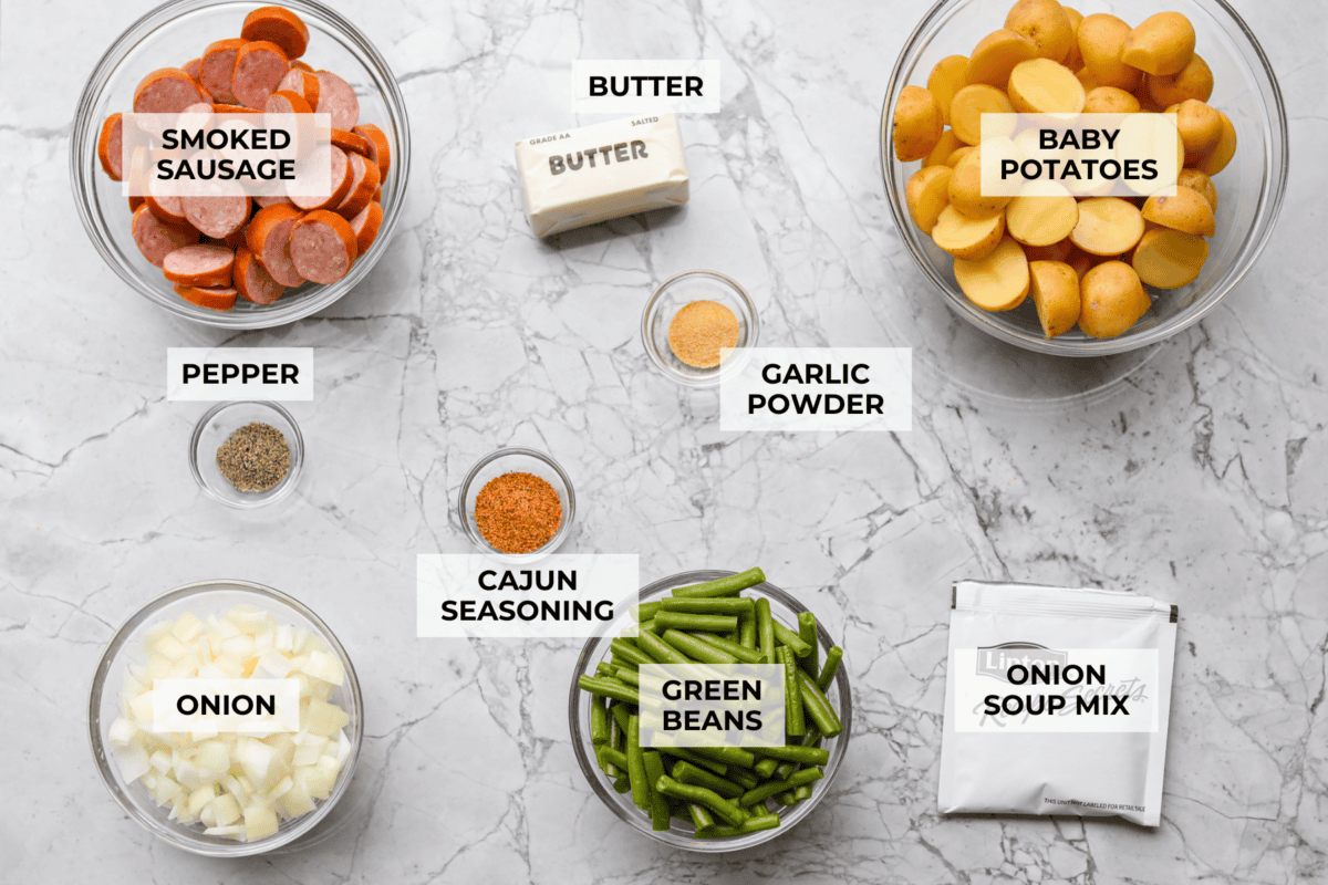 If you haven't tried Swamp Potatoes, you're missing out! This dish is loaded with tender potatoes, smoky sausage, and green beans, all cooked in buttery, savory goodness. Just toss everything in your slow cooker and let it do the work! Overhead shot of labeled swamp potatoes ingredients.