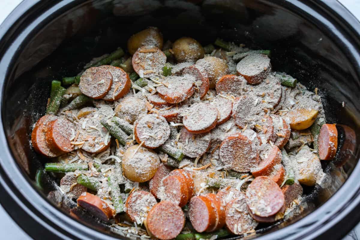 If you haven't tried Swamp Potatoes, you're missing out! This dish is loaded with tender potatoes, smoky sausage, and green beans, all cooked in buttery, savory goodness. Just toss everything in your slow cooker and let it do the work! Seasonings added to the top of the ingredients in the slow cooker.