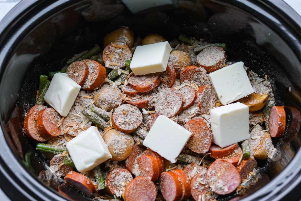 If you haven't tried Swamp Potatoes, you're missing out! This dish is loaded with tender potatoes, smoky sausage, and green beans, all cooked in buttery, savory goodness. Just toss everything in your slow cooker and let it do the work! Cubes of butter added to the top of the seasonings on the other ingredients in the slow cooker.