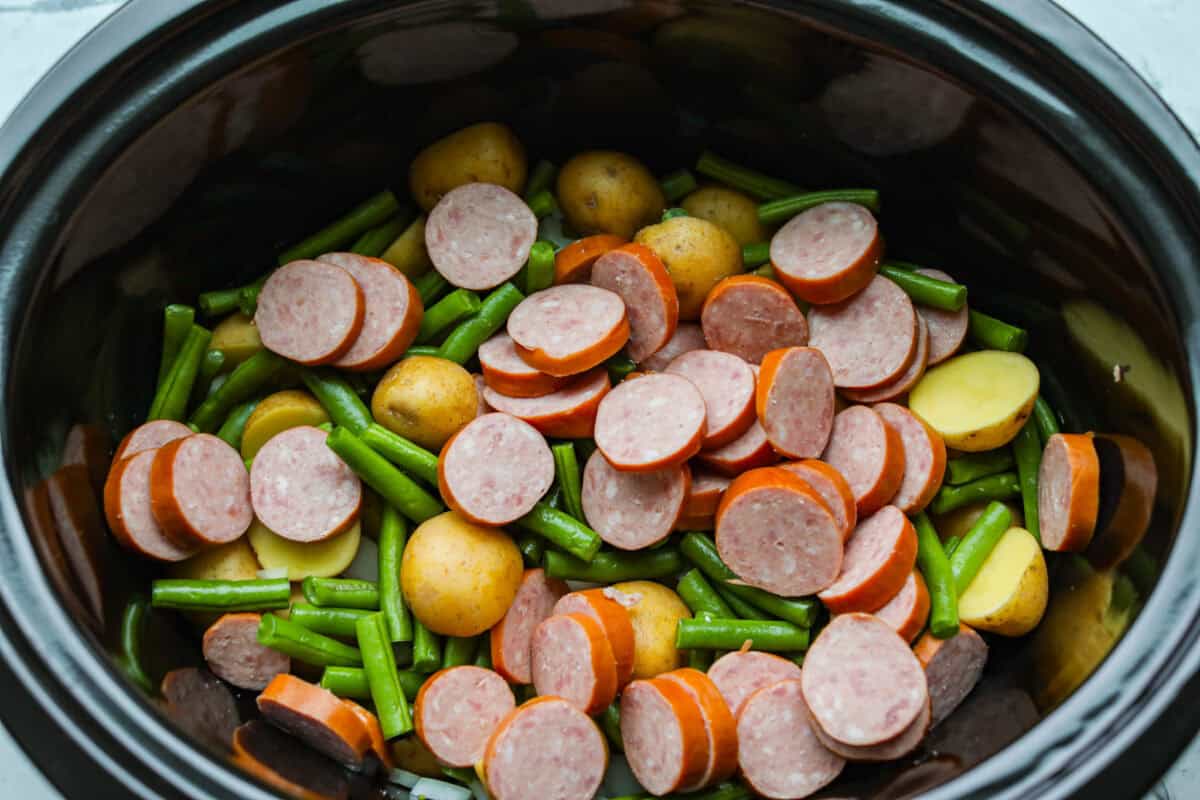 If you haven't tried Swamp Potatoes, you're missing out! This dish is loaded with tender potatoes, smoky sausage, and green beans, all cooked in buttery, savory goodness. Just toss everything in your slow cooker and let it do the work! Sausage and vegetables cut up and added to the slow cooker.