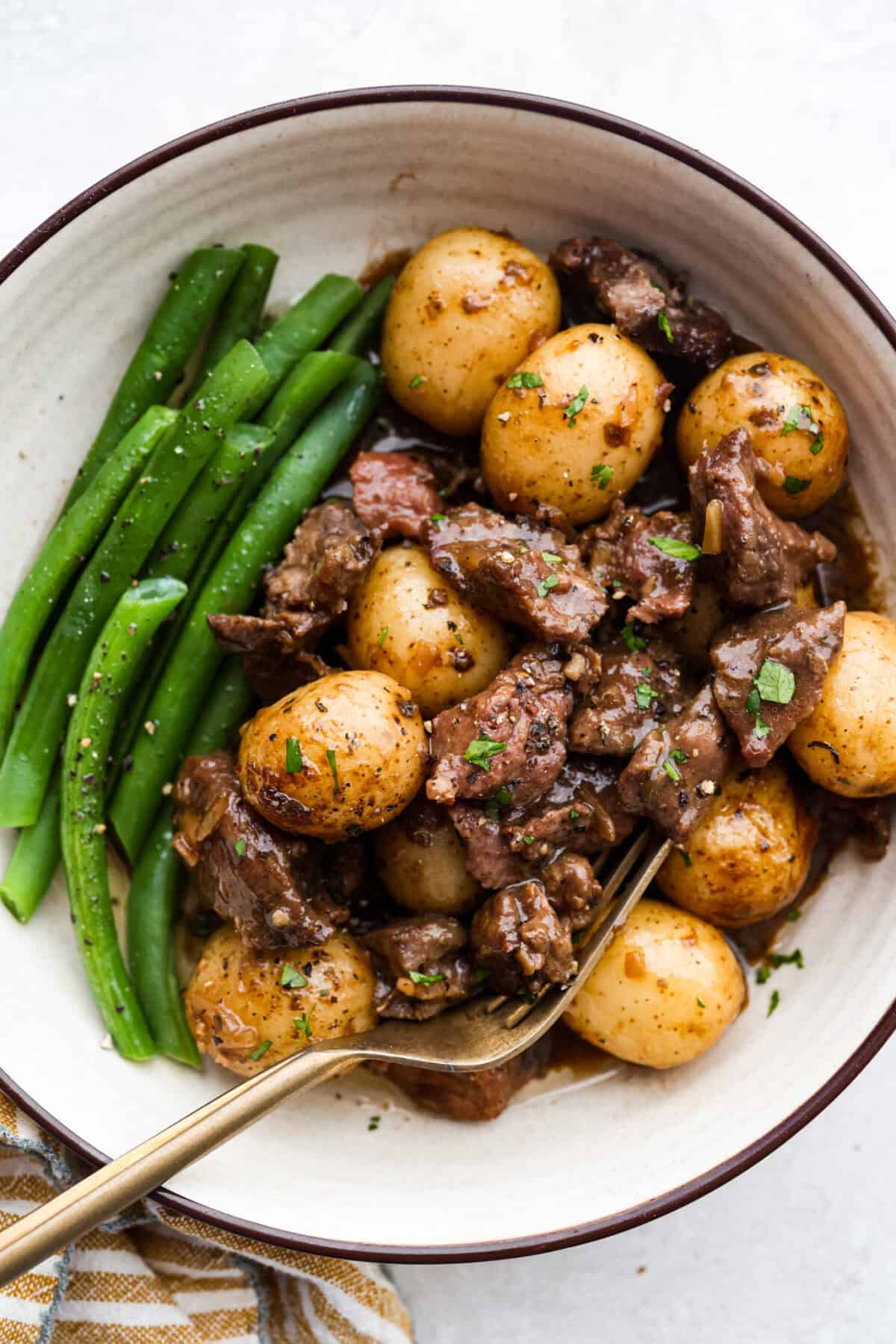 Steak and potatoes are always a good idea, but when the slow cooker does all the work? Even better! This Slow Cooker Steak and Potatoes has melt in your mouth beef, tender, buttery potatoes. And don't even get me started on the delicious savory gravy! Plated green beans and slow cooker steak and potatoes garnished with fresh parsley.