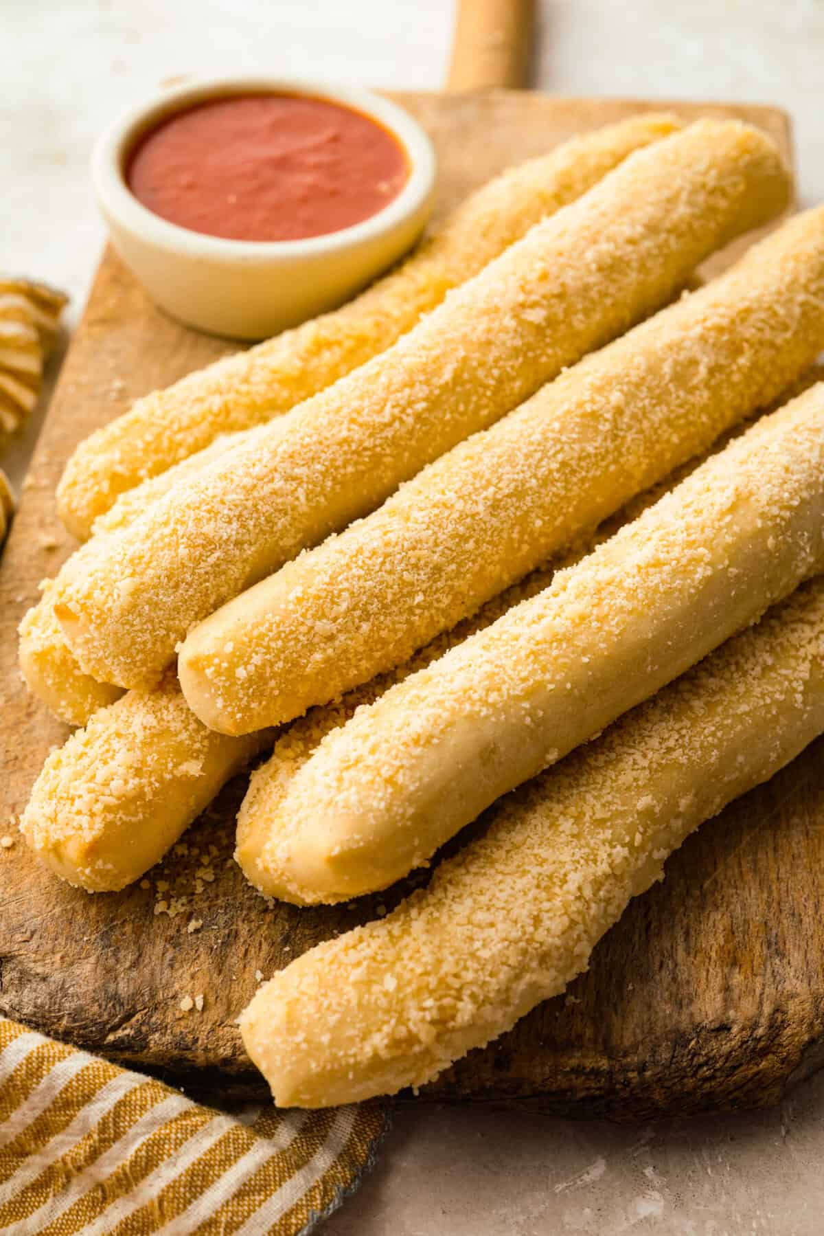 That buttery, garlicky Little Caesars Crazy Bread we all love? You can make it at home, and it's SO good! Soft, fluffy, and covered in Parmesan. Oh, and don't get me started on the garlic butter! Good luck eating just one! Homemade Little Caesars Crazy Bread coated in garlic butter and Parmesan cheese on a wood cutting board with a bowl of marinara next to it.