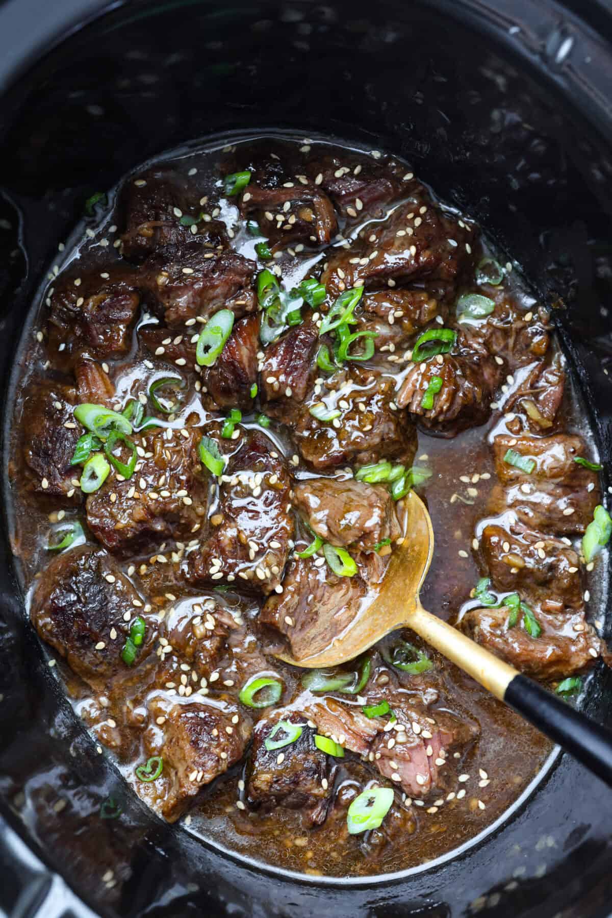 Top down shot of slow cooker sesame ginger beef in a crockpot garnished with sesame seeds and green onions. 