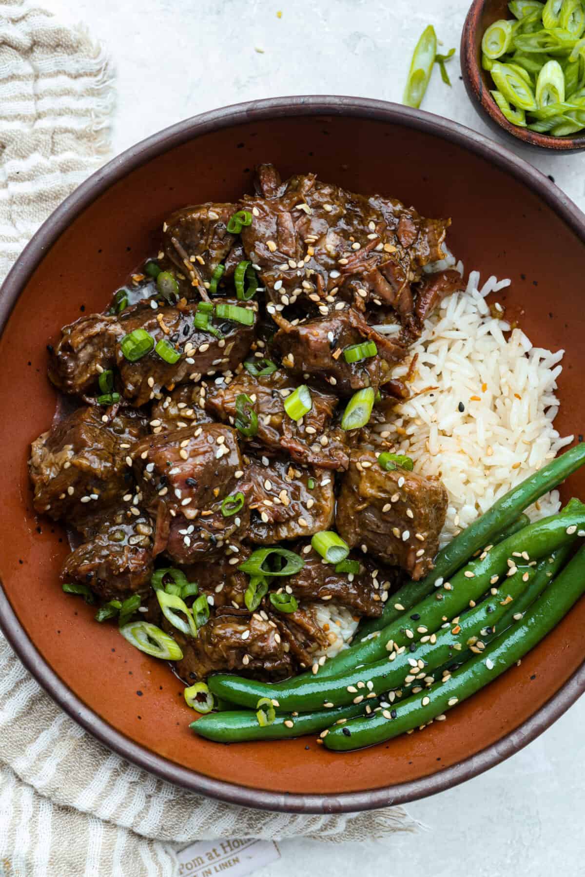 Plated slow cooker sesame ginger beef with rice and green beans.
