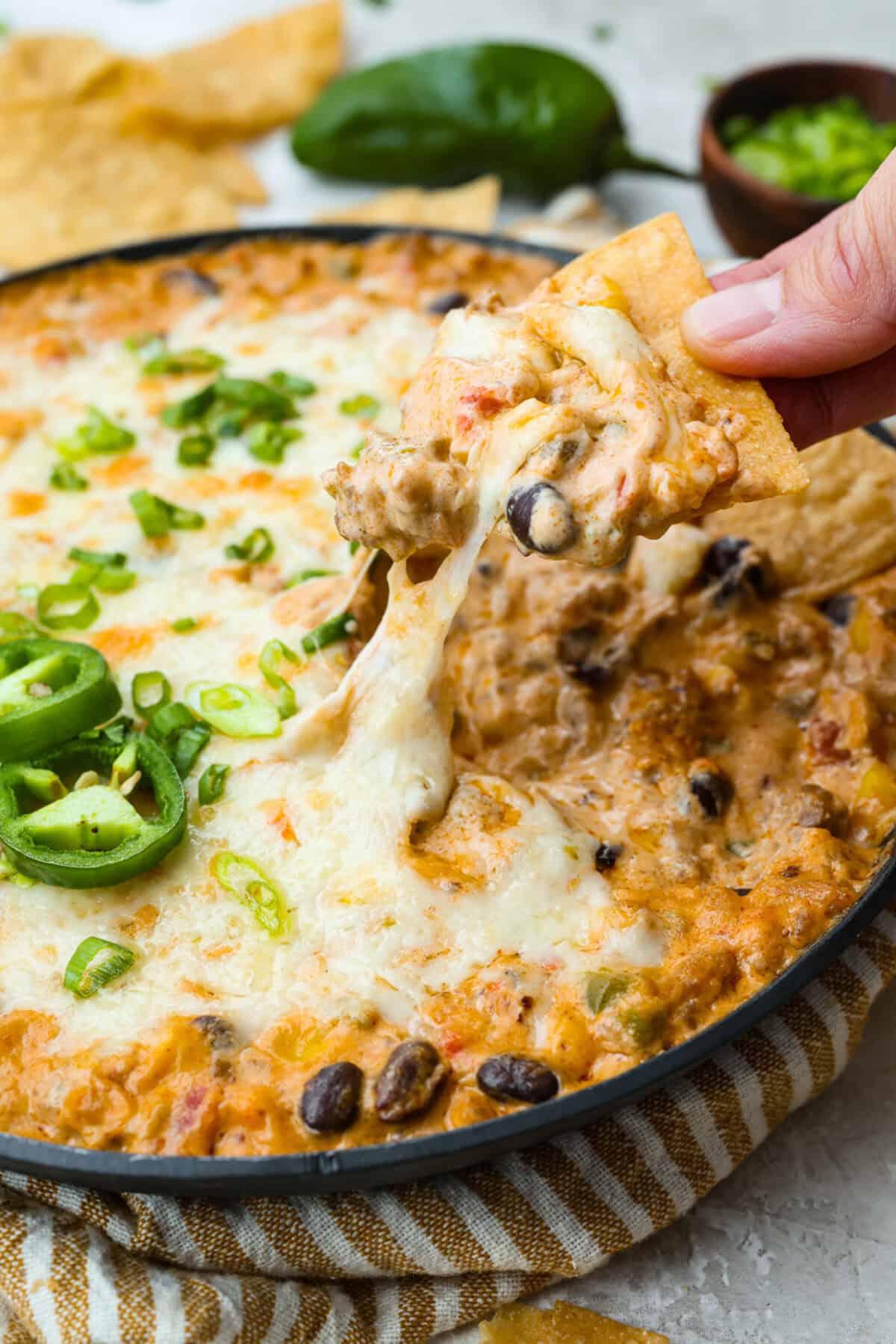 My hot cowboy dip is what I'm bringing to the next game day party! It's loaded with savory sausage, gooey cheese, and a little kick from the jalapeños. Everything comes together in one skillet, so there's less cleanup and more time to dig in! Someone dipping a chip into hot cowboy dip for a cheese pull.