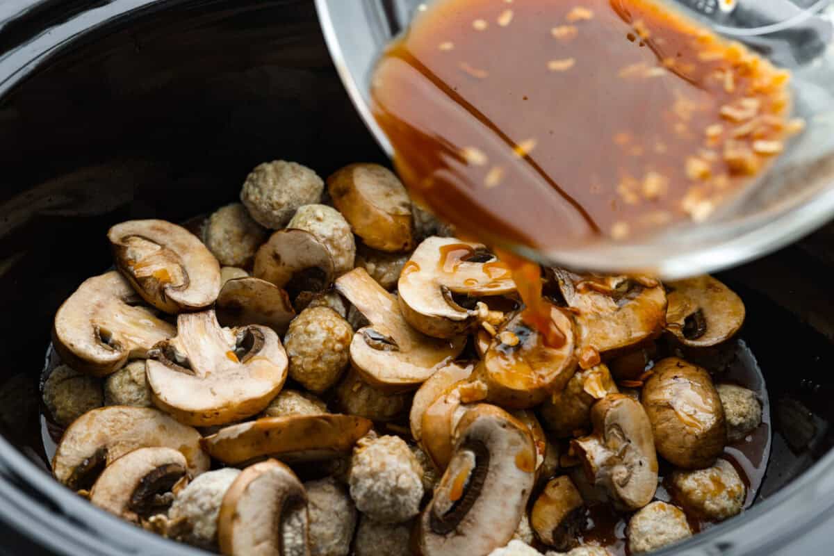 Slow cooker Salisbury steak meatballs are the ultimate comfort food! Tender meatballs and mushrooms simmer in a rich, savory gravy, and the best part? You only need 5 minutes of prep! Sauce being poured over the mushrooms and meatballs.