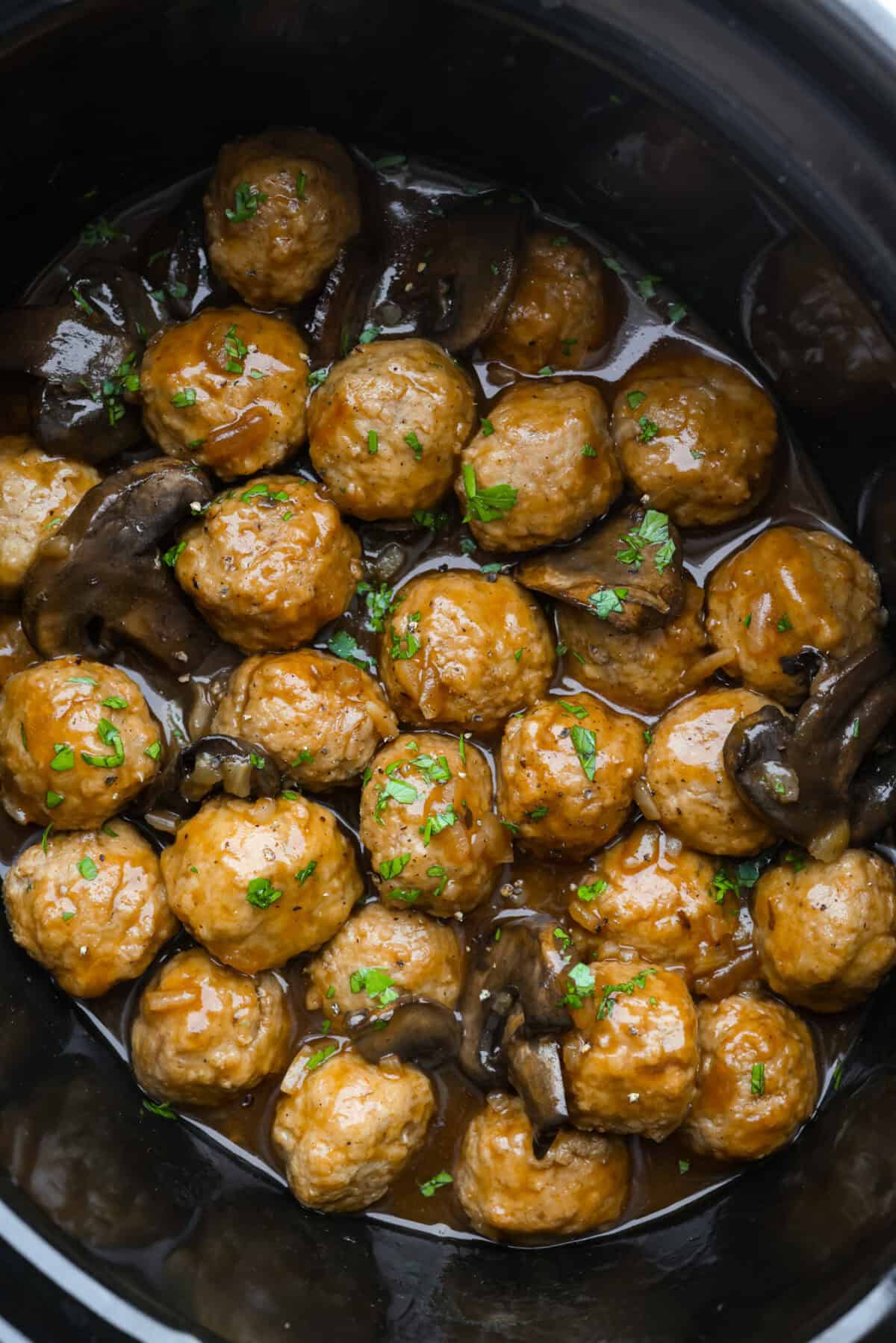 Slow cooker Salisbury steak meatballs are the ultimate comfort food! Tender meatballs and mushrooms simmer in a rich, savory gravy, and the best part? You only need 5 minutes of prep! Slow cooker salisbury meatballs in a slow cooker garnished with parsley.
