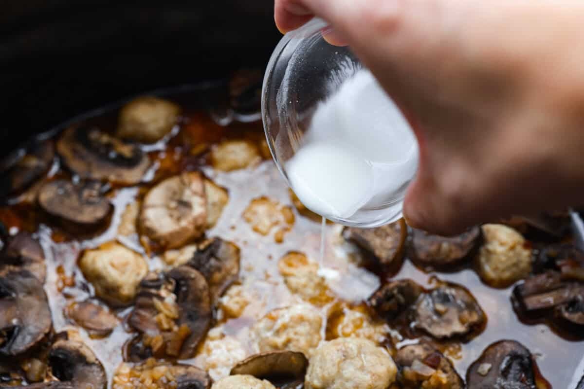 Slow cooker Salisbury steak meatballs are the ultimate comfort food! Tender meatballs and mushrooms simmer in a rich, savory gravy, and the best part? You only need 5 minutes of prep! Cornstarch slurry being poured into the crockpot to thicken the sauce.