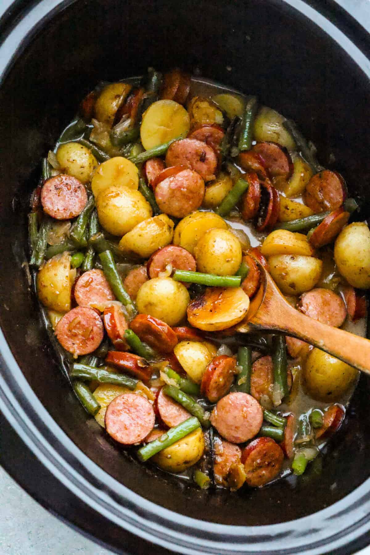 If you haven't tried Swamp Potatoes, you're missing out! This dish is loaded with tender potatoes, smoky sausage, and green beans, all cooked in buttery, savory goodness. Just toss everything in your slow cooker and let it do the work! Slow cooker with cooked and ready to eat swamp potatoes with butter savory sauce and green beans.