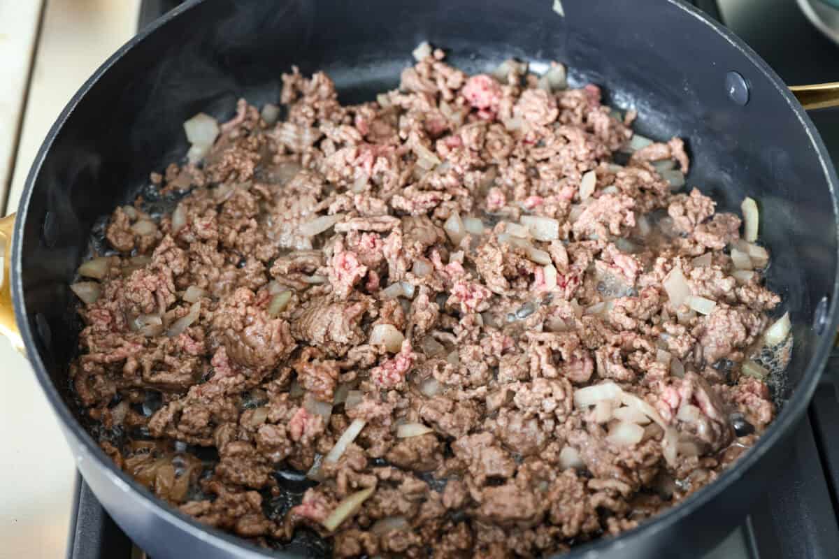 My taco casserole has everything you love about tacos baked into one cheesy, hearty dinner! It's loaded with seasoned ground beef, beans, corn, salsa, and tortilla chips. I love topping mine with sour cream, avocado, and fresh cilantro! Ground beef and onions cooking in a skillet.