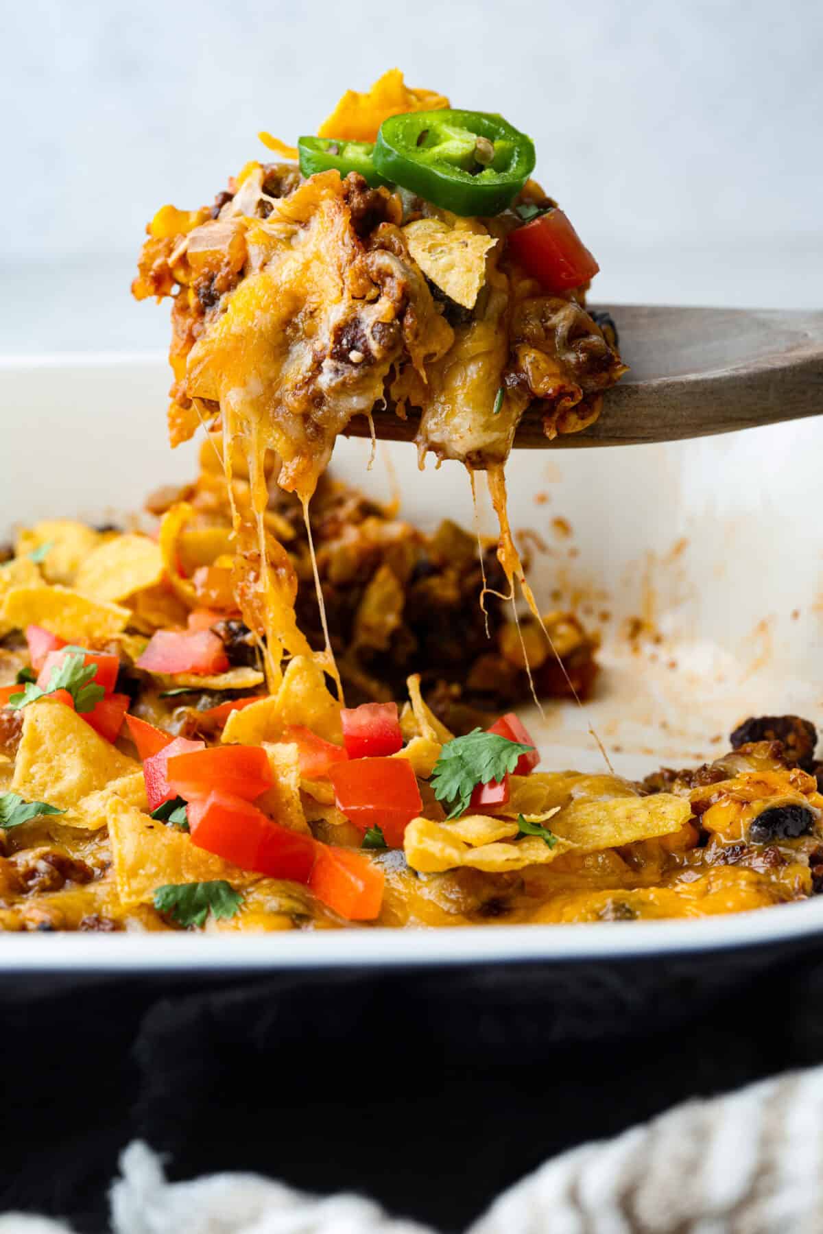 My taco casserole has everything you love about tacos baked into one cheesy, hearty dinner! It's loaded with seasoned ground beef, beans, corn, salsa, and tortilla chips. I love topping mine with sour cream, avocado, and fresh cilantro! Someone scooping a serving of taco casserole out of the baking dish, with a stringy cheese pull.